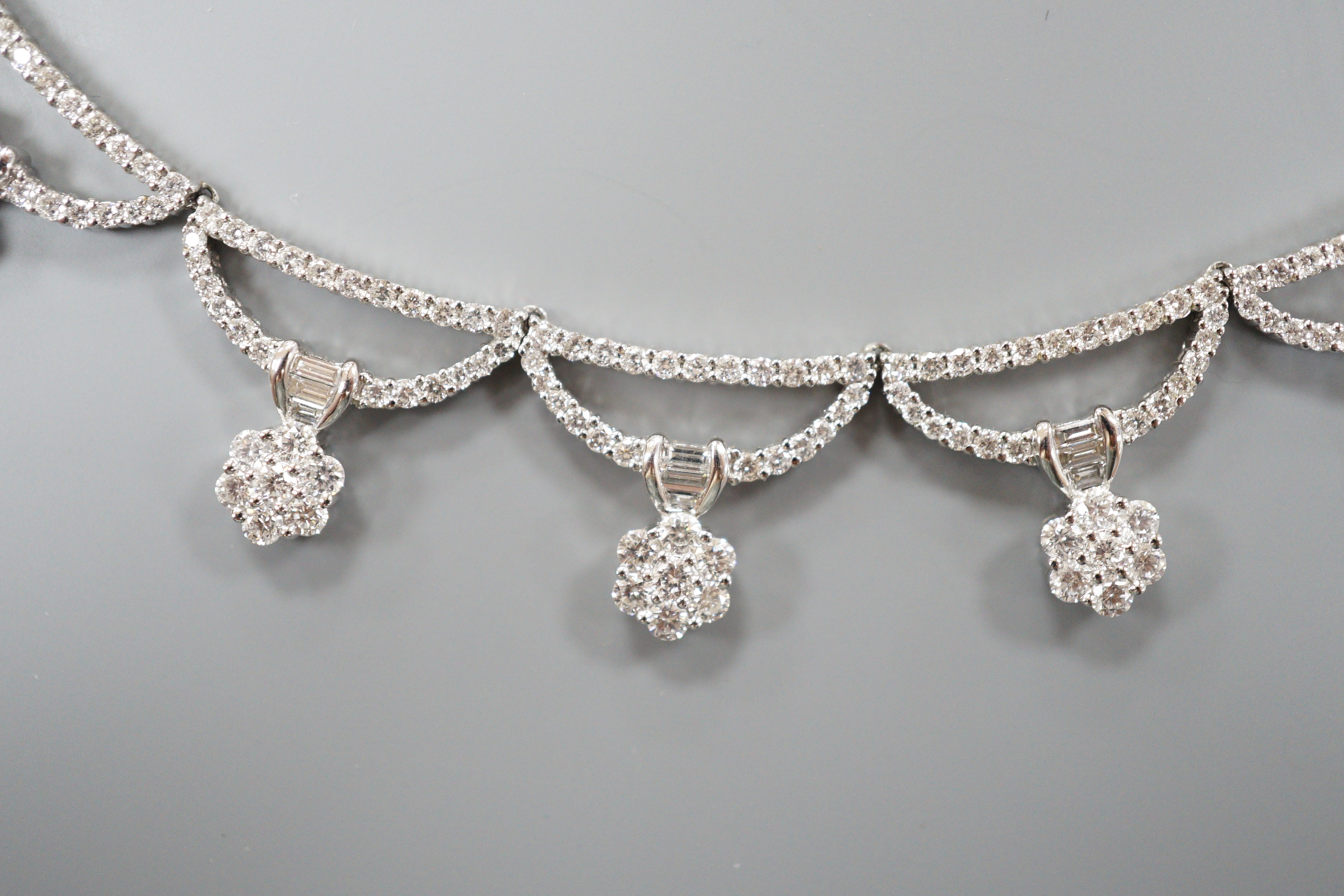A modern 750 white metal and septuple baguette and round cut diamond cluster set curved link fringe necklace, 43cm, gross weight 26.6 grams